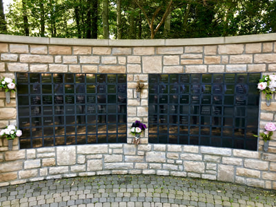 Photo of columbarium wall, a stone wall about 8 feet high with names inscribed on little black plaques.